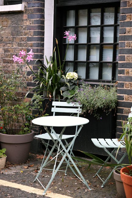 A view of a multi-level interior courtyard featuring a curved green metal railing along the edge of an upstairs walkway. Beneath the balcony, there are lush green plants with broad leaves growing alon